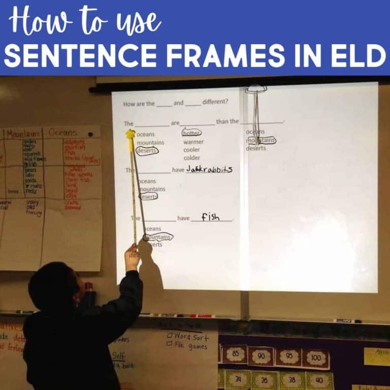 A student points at a projected worksheet about comparing oceans, mountains, and deserts using sentence frames in ELD. Educational posters and charts illustrating Sentence Frames in ELD are visible on the classroom walls.