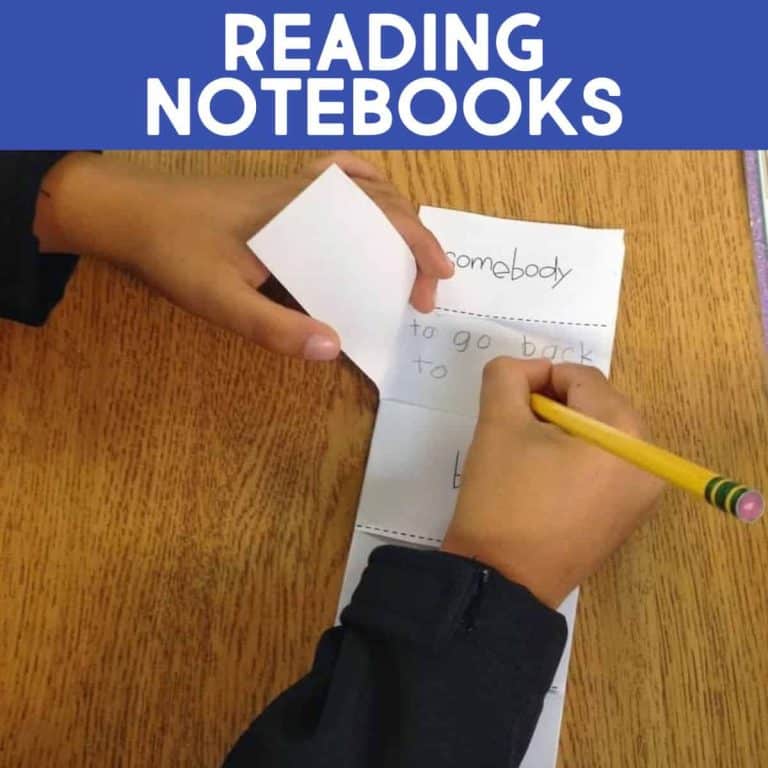 A child writes in a folded Reading Notebook Example with a pencil at a wooden desk. The notebook has handwritten words and a flap being lifted. The text READING NOTEBOOKS is displayed at the top.