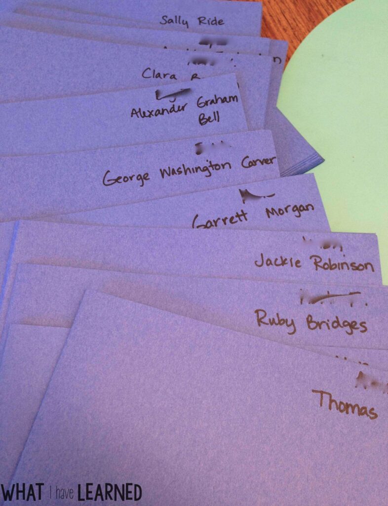A set of stacked purple folders, each labeled with a famous name such as Sally Ride, Clara B., Alexander Graham Bell, George Washington Carver, Garrett Morgan, Jackie Robinson, and Ruby Bridges.