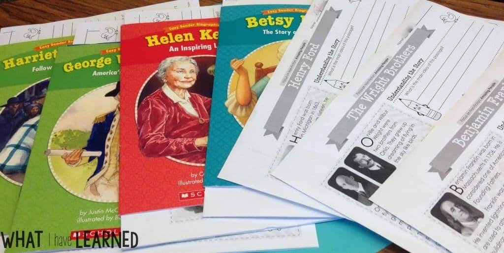 A vibrant set of five biography books about famous figures like Harriet Tubman, Helen Keller, and Benjamin Franklin, along with several black-and-white worksheet pages, are displayed on a table.