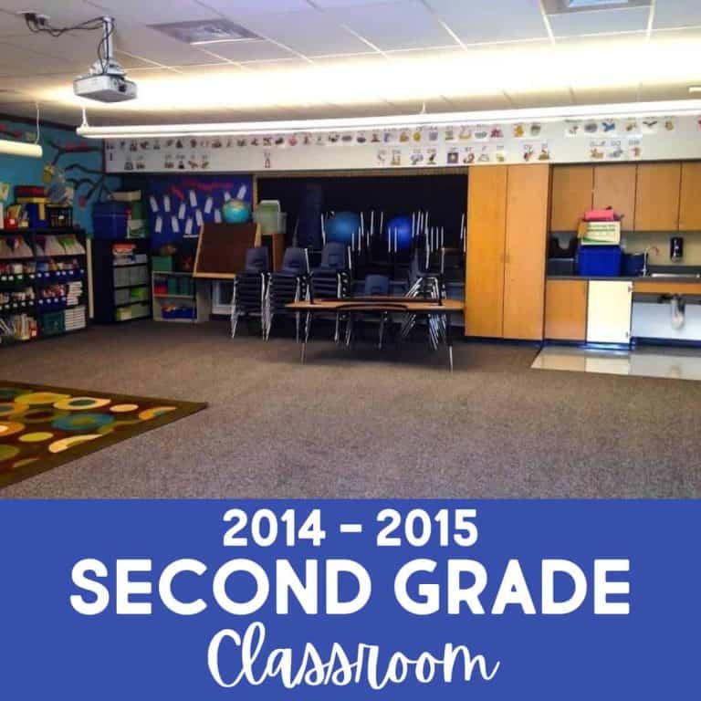 A brightly lit classroom with bookshelves, a rug, and stacked chairs, labeled “2014 - 2015 Second Grade Classroom” at the bottom. The room appears tidy and ready for students.