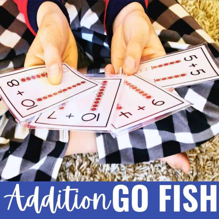 Child in plaid pajamas sits cross-legged on the carpet, holding laminated cards with addition problems and dot visuals. Text at the bottom reads Addition Go Fish Game.