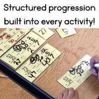 A hand writes answers on a Two-Digit Addition and Subtraction BUNDLE card. Completed cards with handwritten solutions rest on a wooden table. Text above says, Structured progression built into every activity!.