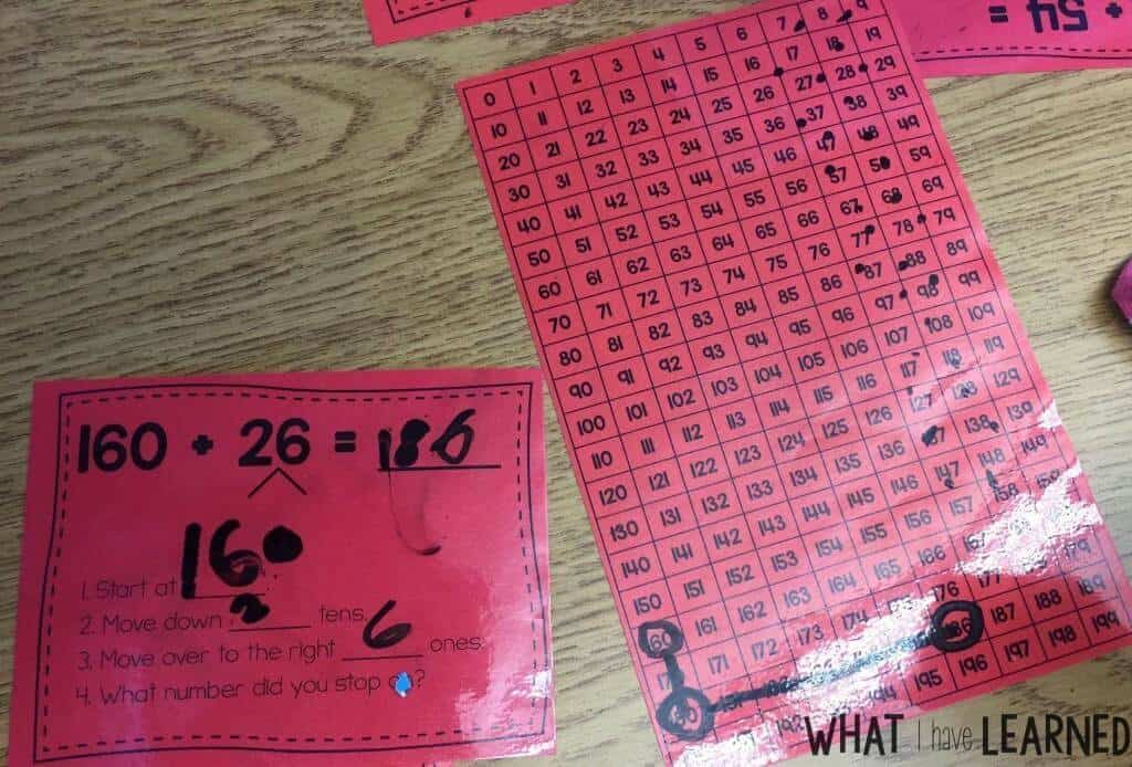 How to Teach a Second Grade Number Line for Addition and Subtraction 2 A red worksheet shows the math problem 160 + 26 = 186 with step-by-step explanations, next to a hundreds chart (1–120). Some numbers are circled, connected by lines, and number lines help illustrate the addition process.