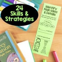 A table displays books, markers, a notebook, and a green Reading Comprehension Bookmark titled “Identify Main Idea & Details.” The bookmark features a diagram, cartoon child, and a black circle stating “24 Skills & Strategies.”.