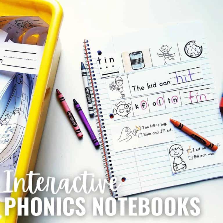 An open Phonics Notebook with exercises, drawings, and simple sentences, surrounded by crayons and a pencil, sits next to a yellow tray of worksheets. Text reads: Interactive PHONICS NOTEBOOKS.