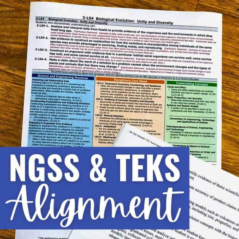 A document comparing NGSS and TEKS science standards sits on a wooden table. Overlapping it is a blue box with bold white text reading “NGSS & TEKS Standards Alignment.”.