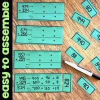 Green math activity cards on a wooden surface show addition problems and breaking numbers into expanded form. Smaller cards with three-digit numbers are scattered nearby. Text on the left reads “easy to assemble.”.