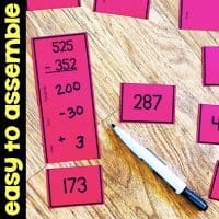 Red math cards display a subtraction problem (525 - 352) broken into steps, with the answer 173. Other cards and a pen are nearby on a wooden surface. A yellow sidebar reads easy to assemble.