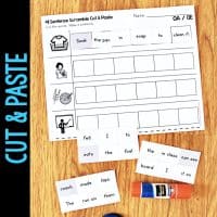 The Long Vowel Teams AI & AY Worksheets & Activities No-Prep Phonics Worksheets are shown on a wooden surface, with word strips and a glue stick nearby. The worksheet includes spaces for assembling sentences using the word strips.