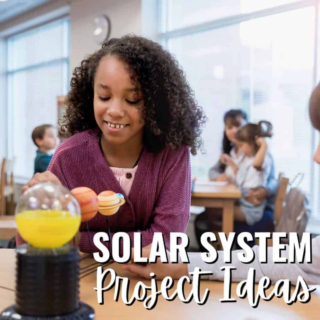 A girl in a classroom smiles while working on a solar system project, with Solar System Project Ideas written in bold white text across the bottom of the image. Other children and an adult are seen blurred in the background.