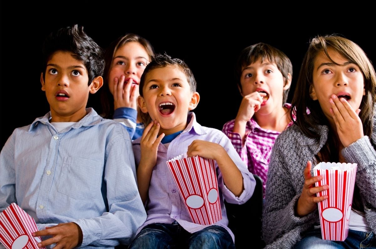 16 Classroom Reward Party Ideas for Elementary Students 3 Five kids sit together, eating popcorn and watching something off-camera with surprised and excited expressions against a black background—offering perfect inspiration for classroom party ideas with the BLOG Movie party.