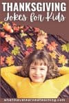 A smiling child in a yellow sweater lies on a wooden floor surrounded by colorful autumn leaves and small pumpkins. Text above reads "Thanksgiving Jokes for Kids"—perfect for families searching for fun thanksgiving jokes for kids.